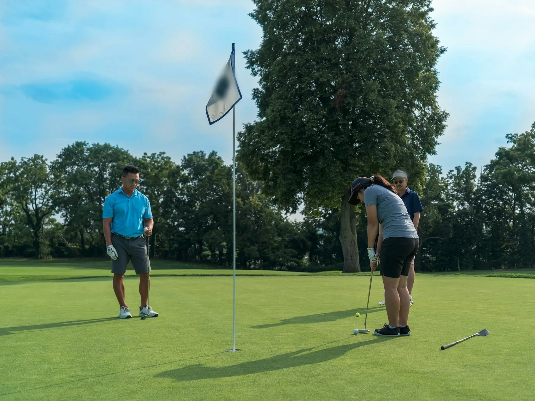 Three golfers on a putting green, one lining up a putt beside the flag