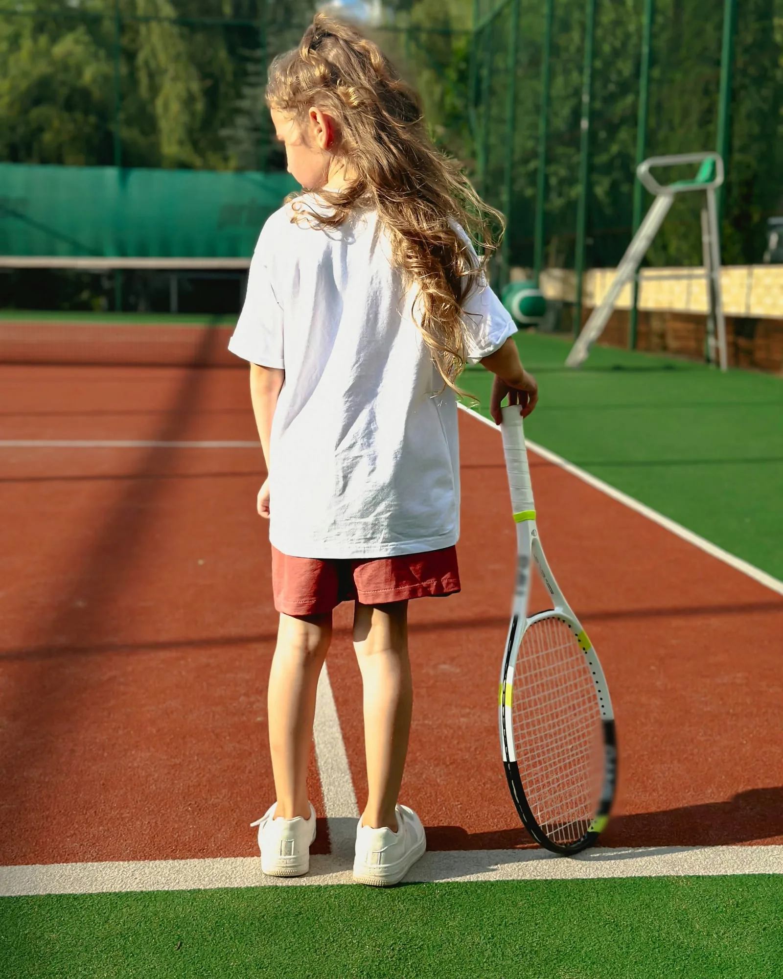 A young tennis player on a red tennis court, racquet resting at her side