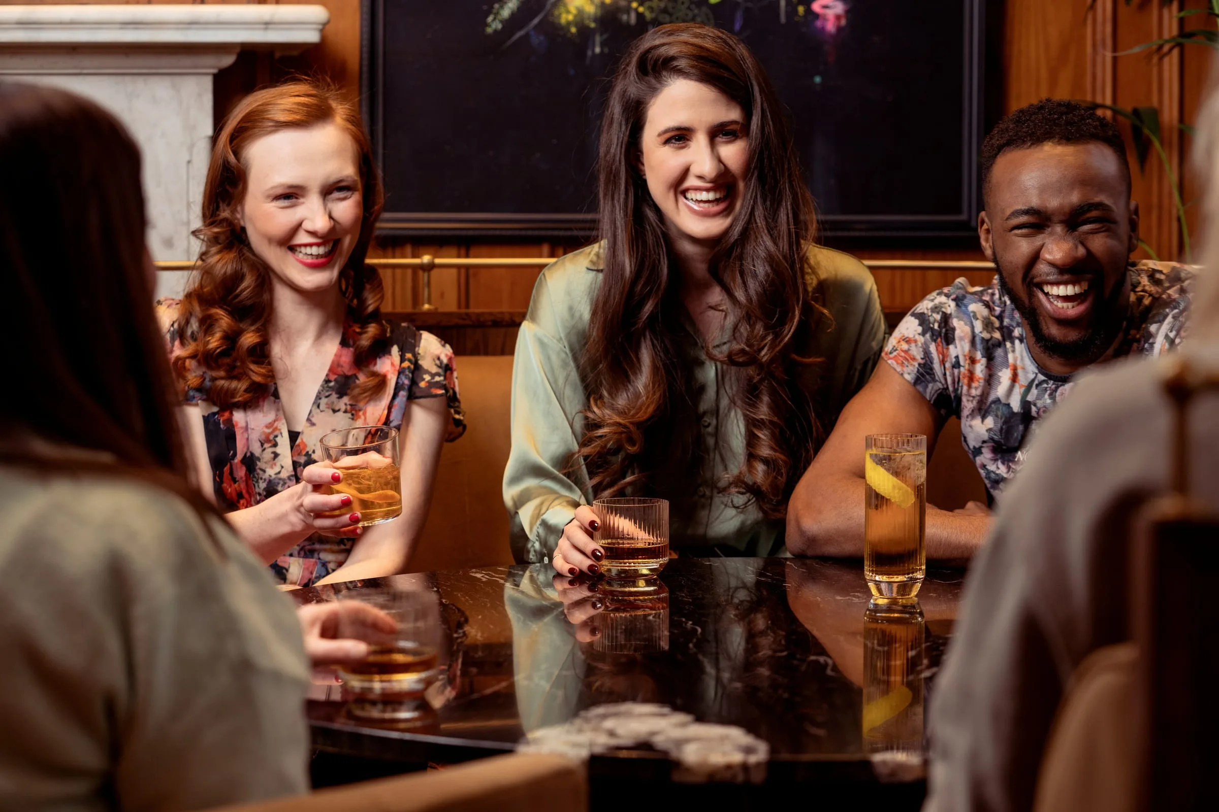 Friends laughing around a marble table with drinks in a wood-panelled bar