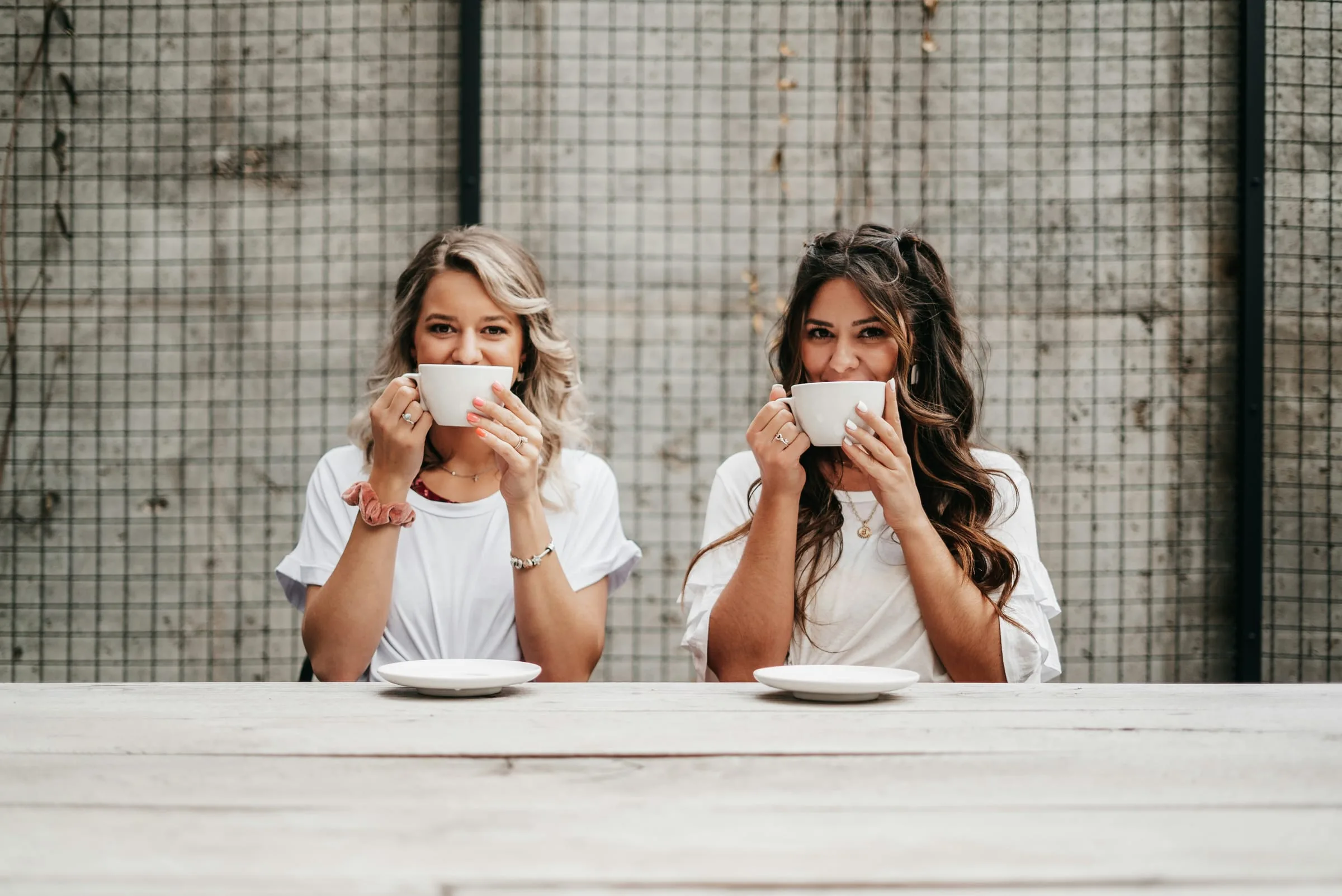 Two friends drinking coffee at a long wooden table