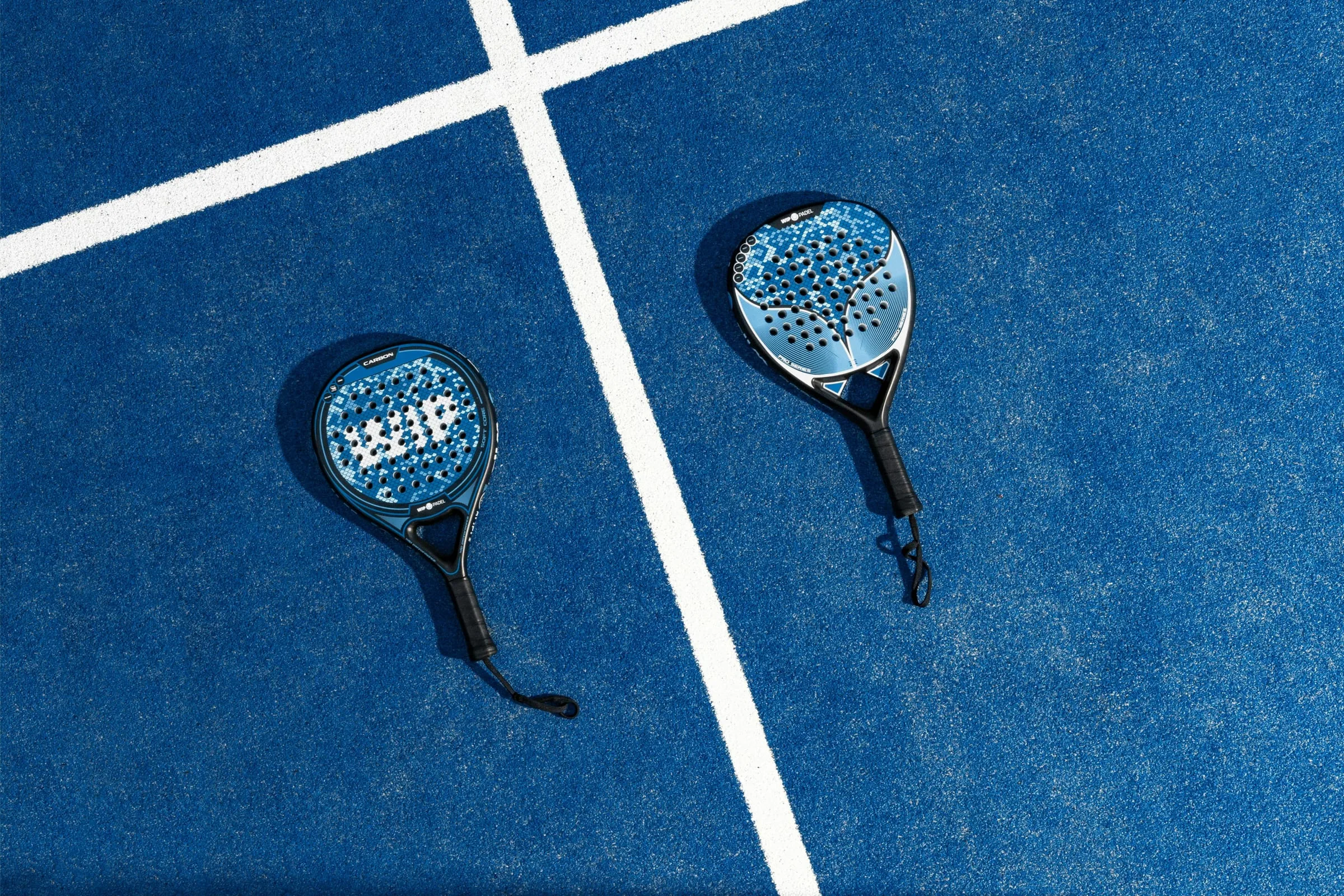 Two padel racquets lying on a deep blue court beside white lines