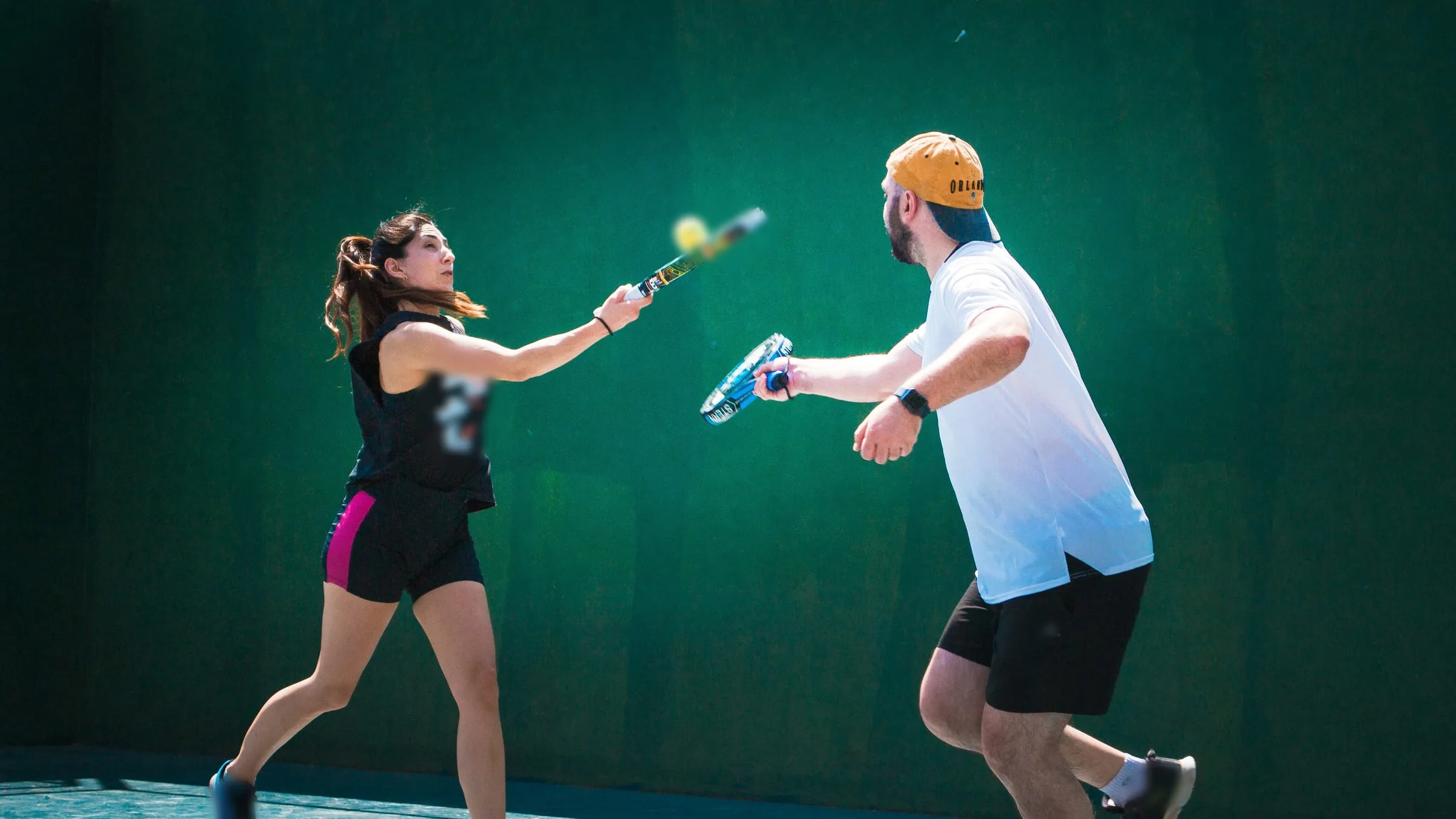 Two padel players rallying at the net in front of a green wall